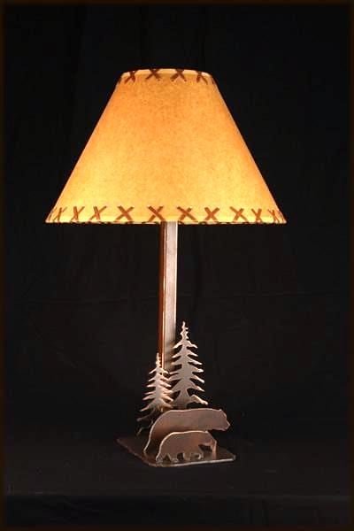 May include: A table lamp with a brown and tan lampshade and a metal base featuring a silhouette of two bears walking through a forest of trees.
